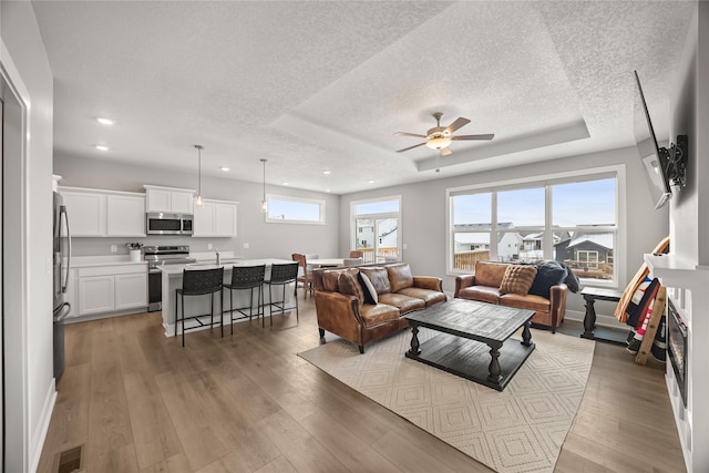 living room featuring a textured ceiling, a tray ceiling, ceiling fan, sink, and light hardwood / wood-style flooring