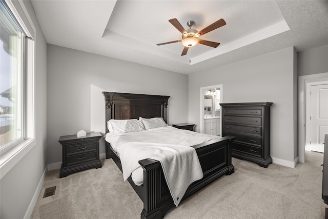 carpeted bedroom with ensuite bath, ceiling fan, and a tray ceiling