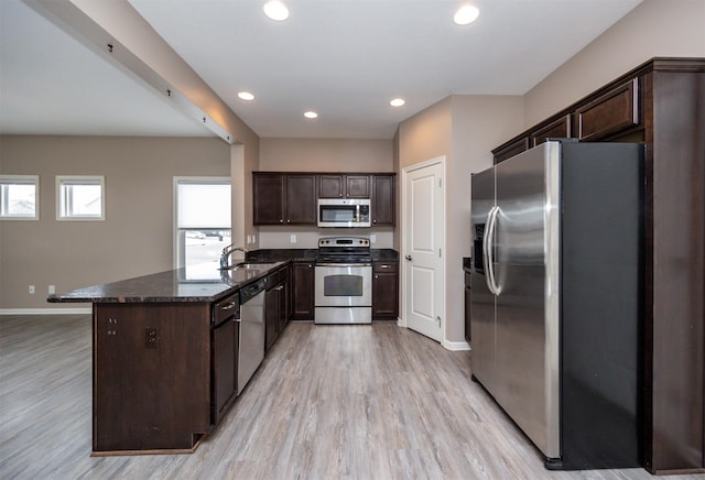 kitchen with light hardwood / wood-style floors, dark stone countertops, dark brown cabinetry, and appliances with stainless steel finishes