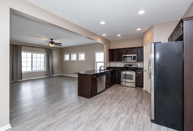 kitchen with kitchen peninsula, appliances with stainless steel finishes, light wood-type flooring, dark brown cabinetry, and sink