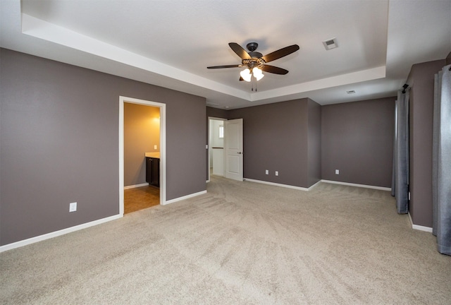 unfurnished bedroom with ceiling fan, a raised ceiling, light colored carpet, and ensuite bathroom