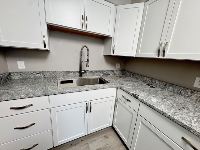 kitchen featuring white cabinetry, sink, light stone countertops, and light hardwood / wood-style floors