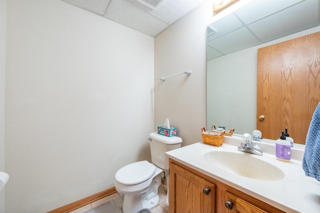 half bathroom featuring a drop ceiling, baseboards, toilet, and vanity