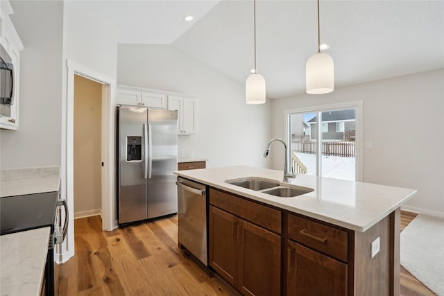 kitchen with lofted ceiling, a kitchen island with sink, hanging light fixtures, sink, and appliances with stainless steel finishes