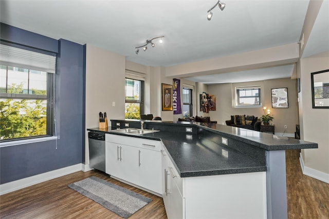 kitchen featuring dark countertops, dark wood finished floors, a peninsula, and stainless steel dishwasher