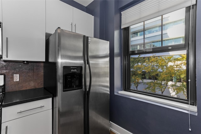 kitchen featuring tasteful backsplash, dark countertops, stainless steel fridge with ice dispenser, white cabinets, and baseboards