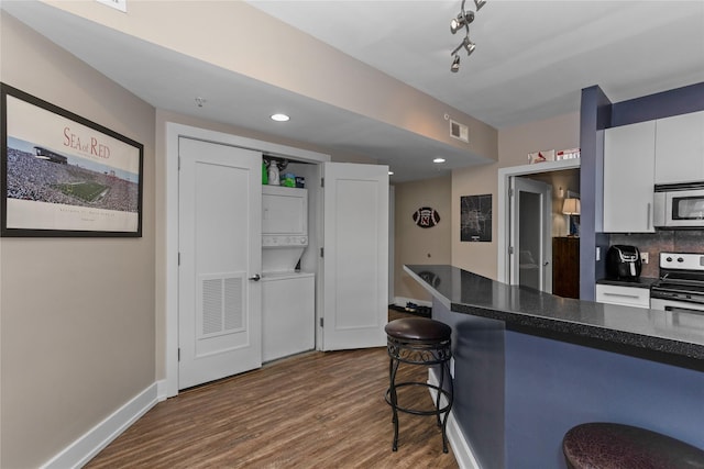 kitchen with visible vents, dark countertops, appliances with stainless steel finishes, stacked washing maching and dryer, and a kitchen bar