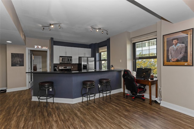 kitchen featuring appliances with stainless steel finishes, dark countertops, white cabinets, and a kitchen bar