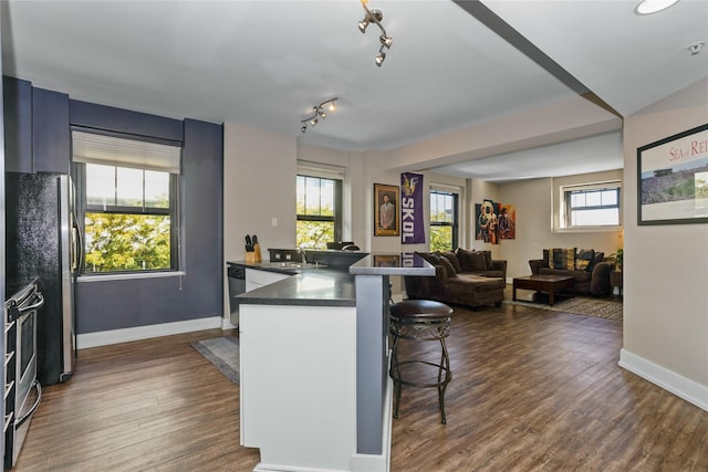 kitchen with a peninsula, a sink, a kitchen breakfast bar, dark countertops, and plenty of natural light