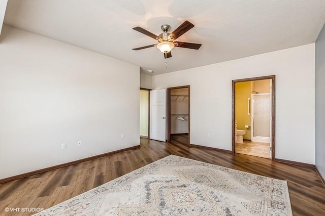 unfurnished bedroom with connected bathroom, ceiling fan, dark hardwood / wood-style floors, a walk in closet, and a closet