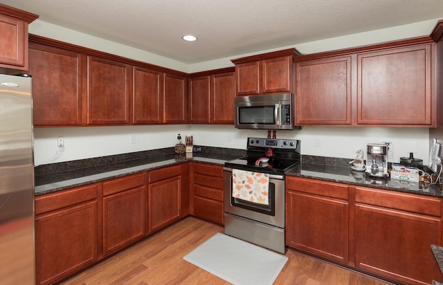 kitchen with a textured ceiling, light wood-type flooring, stainless steel appliances, and dark stone counters