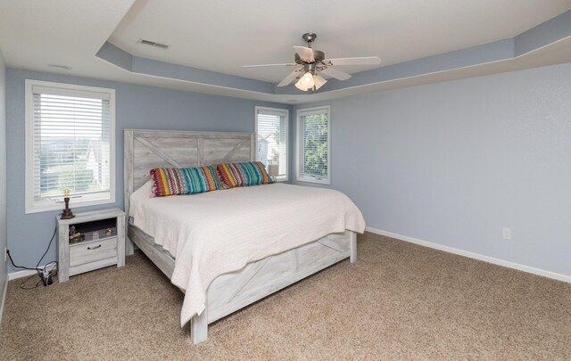 carpeted bedroom with ceiling fan and a tray ceiling