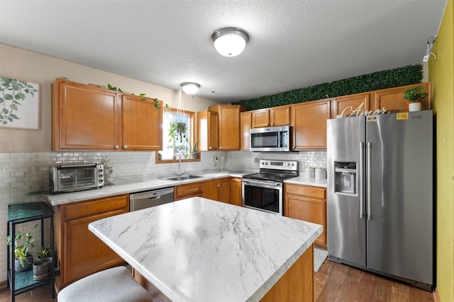 kitchen with dark hardwood / wood-style flooring, a textured ceiling, stainless steel appliances, sink, and a kitchen island