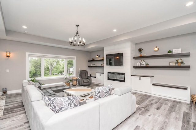 living room with a tray ceiling, a large fireplace, a chandelier, and light hardwood / wood-style flooring