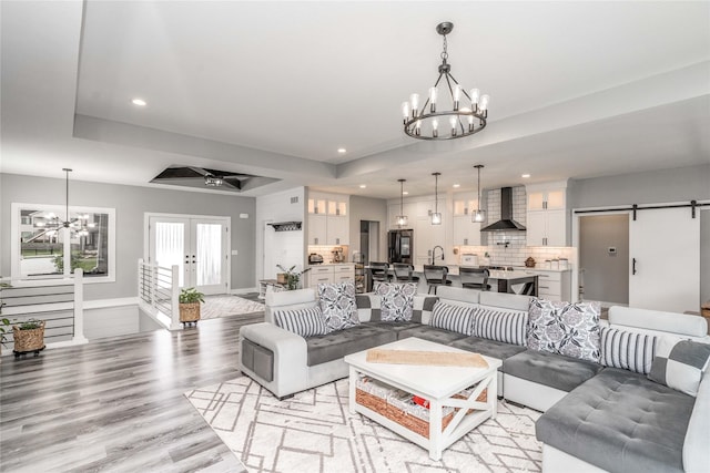 living room featuring french doors, sink, a barn door, a tray ceiling, and light hardwood / wood-style floors