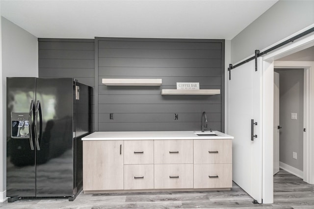 kitchen featuring a barn door, black fridge with ice dispenser, light hardwood / wood-style flooring, and sink