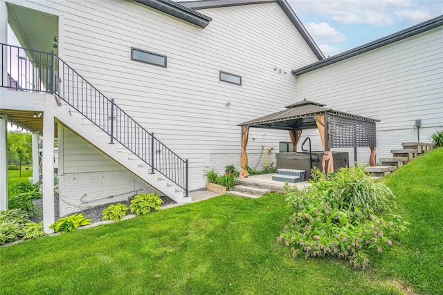 rear view of property with a gazebo, a hot tub, and a lawn