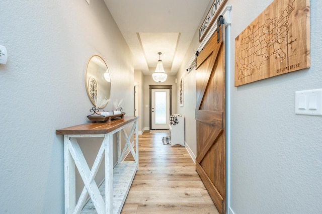 hall with light wood-style flooring, baseboards, and a barn door