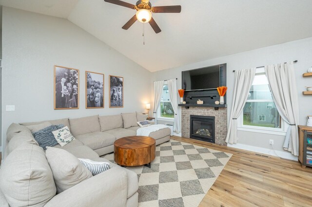 living room featuring ceiling fan, lofted ceiling, light hardwood / wood-style flooring, and a brick fireplace