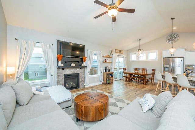 living room featuring a brick fireplace, light wood-style flooring, vaulted ceiling, and ceiling fan