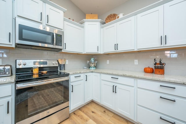 kitchen featuring white cabinets, light stone counters, appliances with stainless steel finishes, light wood-style floors, and backsplash