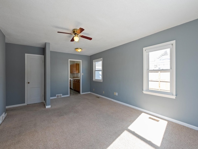 unfurnished bedroom featuring a textured ceiling, ceiling fan, light carpet, and ensuite bath