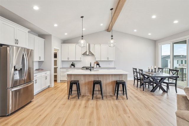 kitchen featuring wall chimney range hood, stainless steel fridge with ice dispenser, an island with sink, tasteful backsplash, and white cabinetry