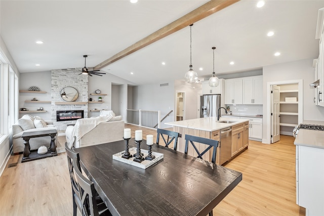 dining room with a fireplace, light wood-type flooring, vaulted ceiling with beams, and sink