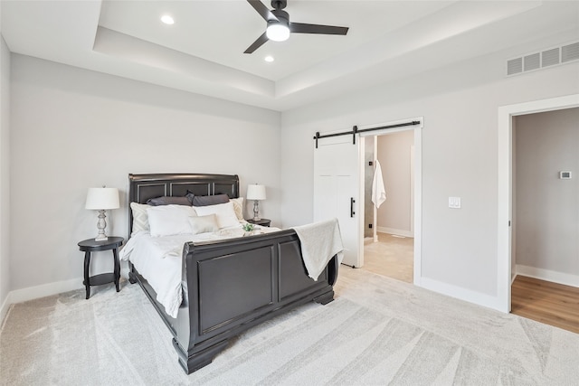 carpeted bedroom with a raised ceiling, a barn door, and ceiling fan