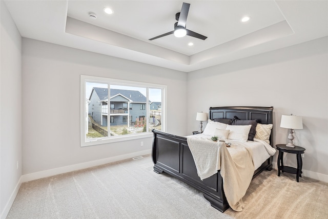 bedroom with a raised ceiling, ceiling fan, and light carpet