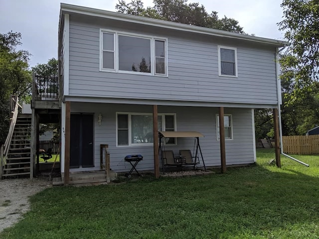 back of property with fence, a lawn, and stairway