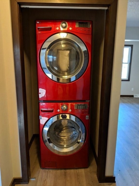 laundry room featuring baseboards, laundry area, stacked washer / dryer, and wood finished floors