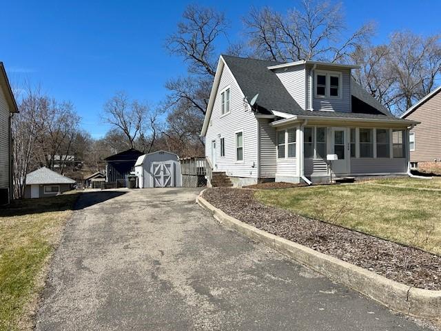 view of front of house with a shingled roof, a front yard, a storage shed, an outdoor structure, and driveway