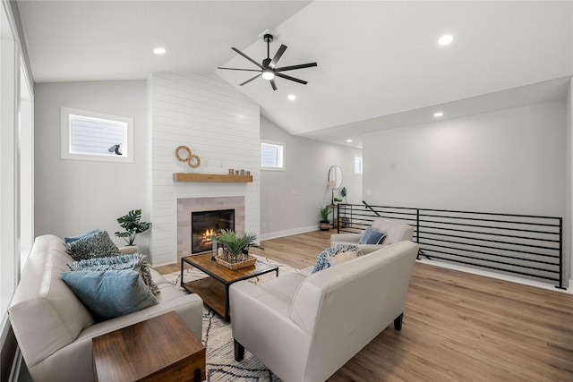 living room with ceiling fan, light wood-type flooring, a fireplace, and vaulted ceiling