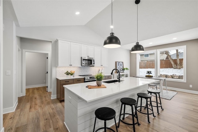 kitchen featuring decorative backsplash, appliances with stainless steel finishes, sink, white cabinets, and an island with sink