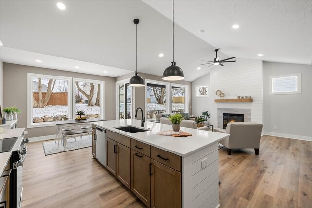 kitchen with pendant lighting, a center island with sink, sink, a fireplace, and appliances with stainless steel finishes