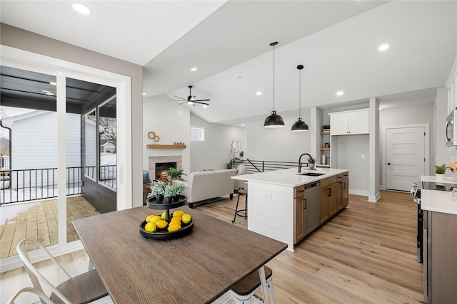 kitchen with vaulted ceiling, sink, decorative light fixtures, a center island with sink, and white cabinetry