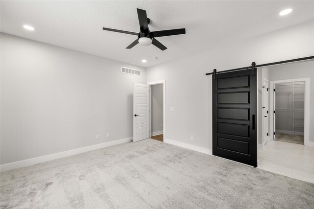 unfurnished bedroom with light carpet, a walk in closet, ceiling fan, a barn door, and a closet