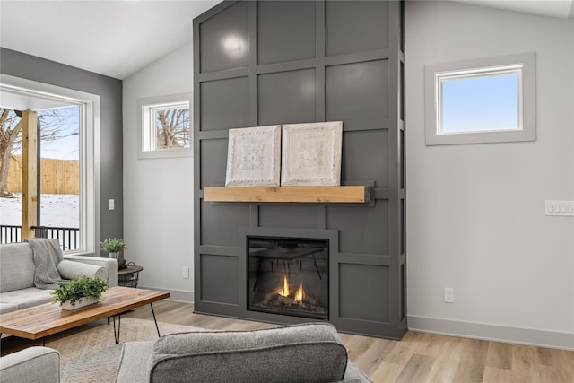 living room with a large fireplace, light hardwood / wood-style floors, and vaulted ceiling