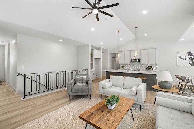 living room with light hardwood / wood-style floors, vaulted ceiling, ceiling fan, and sink