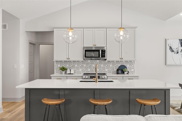 kitchen with pendant lighting, lofted ceiling, backsplash, and an island with sink