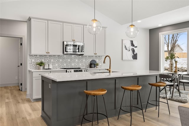 kitchen with a kitchen island with sink, sink, decorative light fixtures, and light wood-type flooring