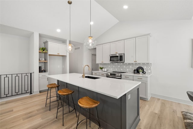 kitchen featuring lofted ceiling, hanging light fixtures, sink, an island with sink, and stainless steel appliances