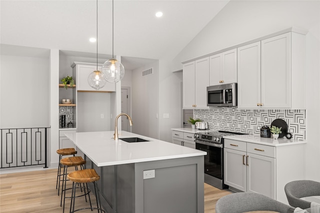 kitchen with sink, pendant lighting, lofted ceiling, a center island with sink, and range