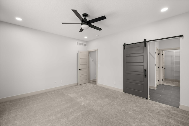 unfurnished bedroom with ceiling fan, a barn door, and dark carpet