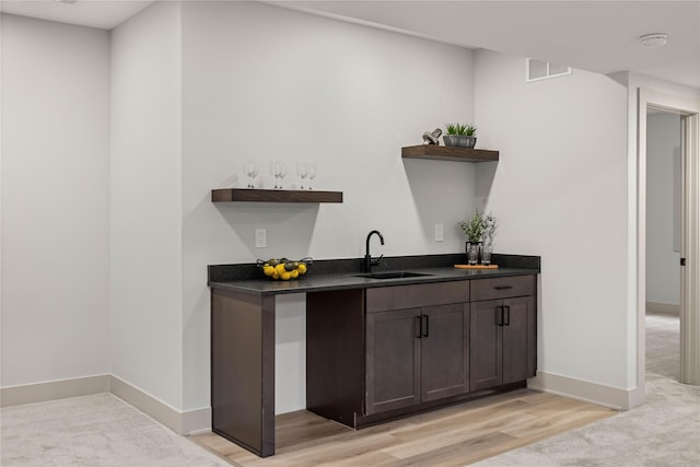 bar with dark brown cabinetry, light hardwood / wood-style flooring, and sink