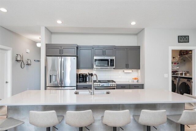 kitchen with tasteful backsplash, stainless steel appliances, a spacious island, sink, and washing machine and clothes dryer