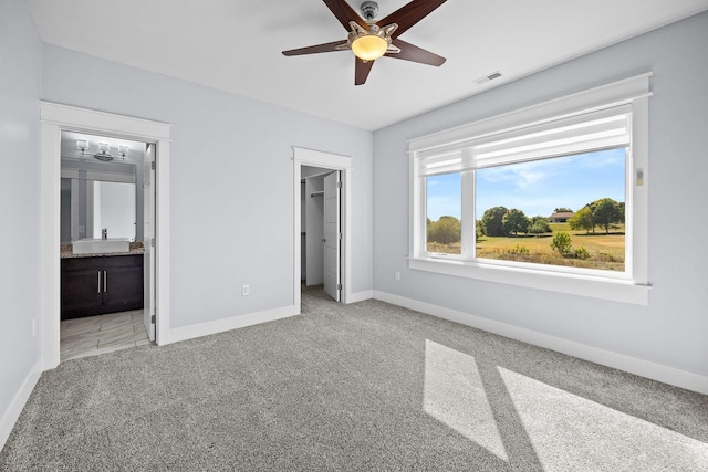 unfurnished bedroom with light carpet, ensuite bathroom, a walk in closet, ceiling fan, and a closet