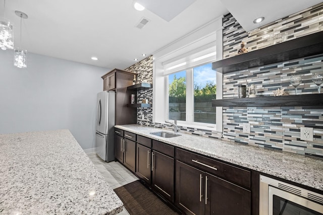 kitchen featuring decorative backsplash, light stone countertops, stainless steel appliances, sink, and hanging light fixtures