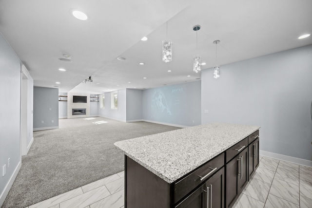 kitchen with pendant lighting, light stone countertops, dark brown cabinets, a kitchen island, and light colored carpet